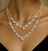 Two layered diamond-studded leaf-pattern necklaces forming a V on a model's neck.